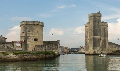 The two medieval stone towers at the entrance to La Rochelle's old harbour, reflected in calm water under a blue sky