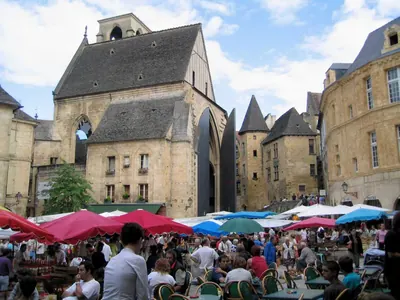 Market stalls and café tables on place de la Liberté in Sarlat, in front of the old Sainte-Marie church