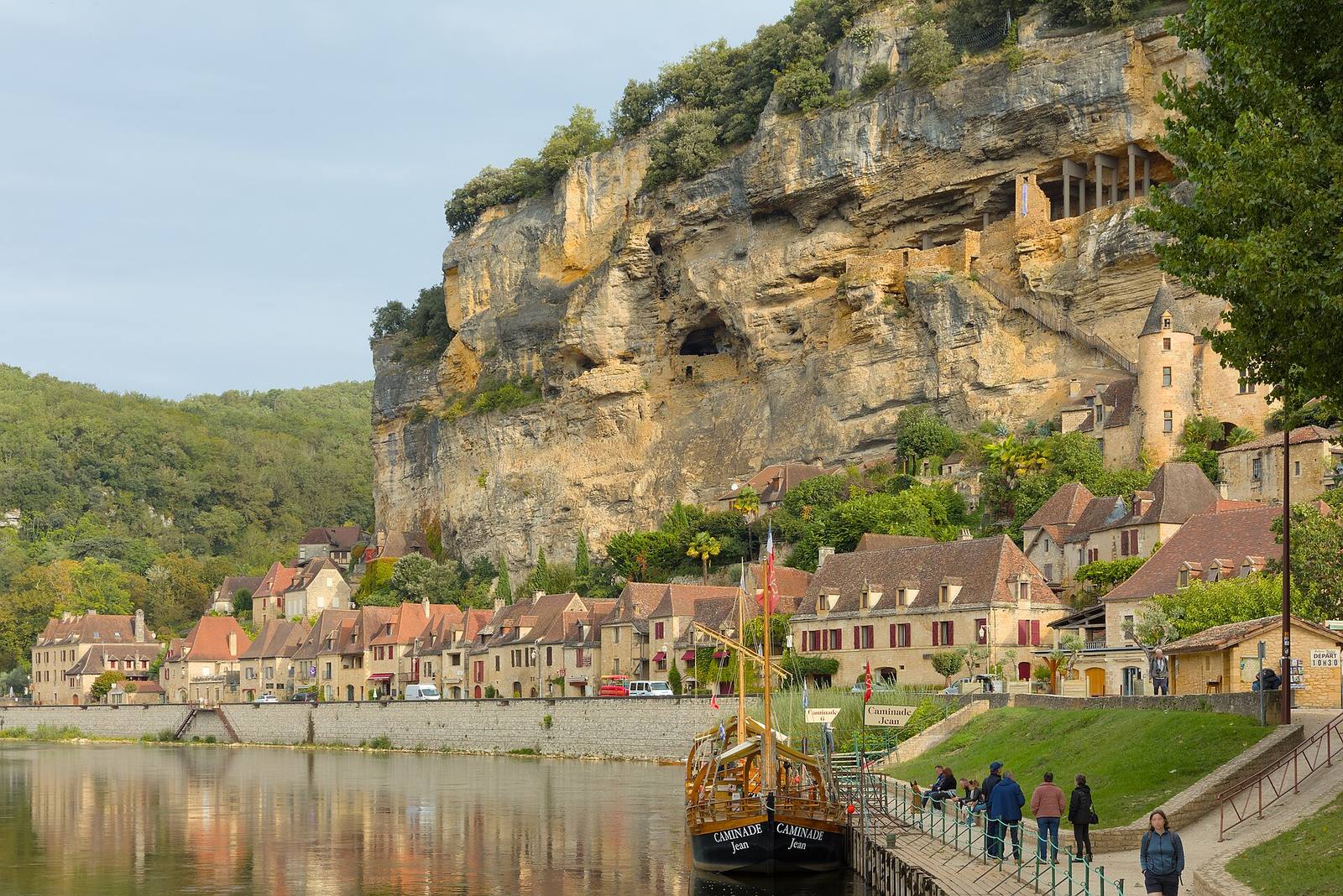 La Roque-Gageac: stone houses along the Dordogne below a tall cliff, with a gabarre moored at the river bank
